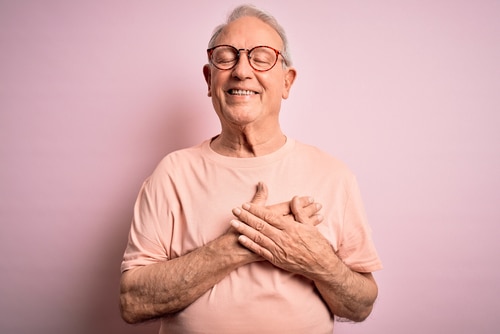 senior man with hands on chest with closed eyes and grateful gesture on face.