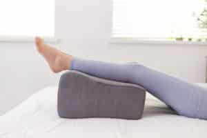 A woman in leggings lying in bed resting with a cushion on her feet.