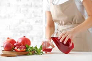 Woman pouring fresh pomegranate juice into glass in kitchen
